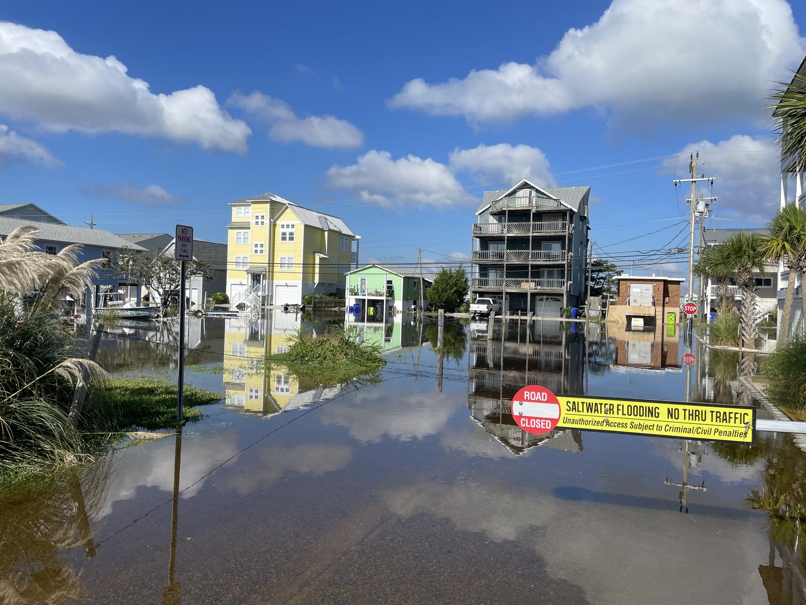 Saltwater flooding on a residential street in Carolina Beach, NC, with a 'Road Closed: Saltwater Flooding, No Thru Traffic' sign in the foreground